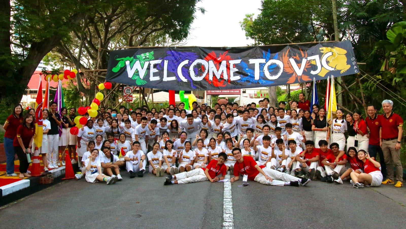 Large group of students and staff posing under a colorful Welcome to VJC banner on a road.